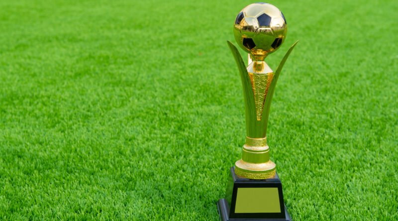 Messi mejor jugador: trofeos de fútbol apoyados sobre el césped de una cancha