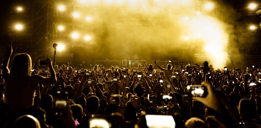 Público de espaldas con celulares frente a un escenario, ilustra los shows de Ricardo Arjona