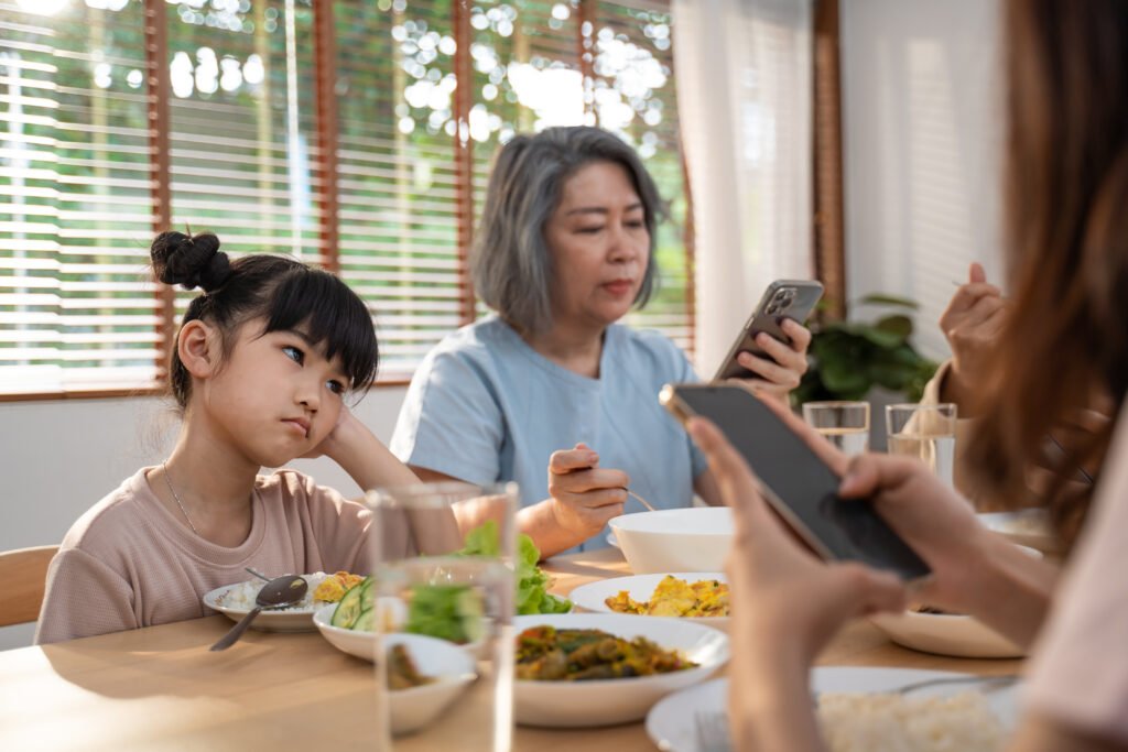 uso del celular: familia absorta en el teléfono en la mesa mientras una adolescente se aburre