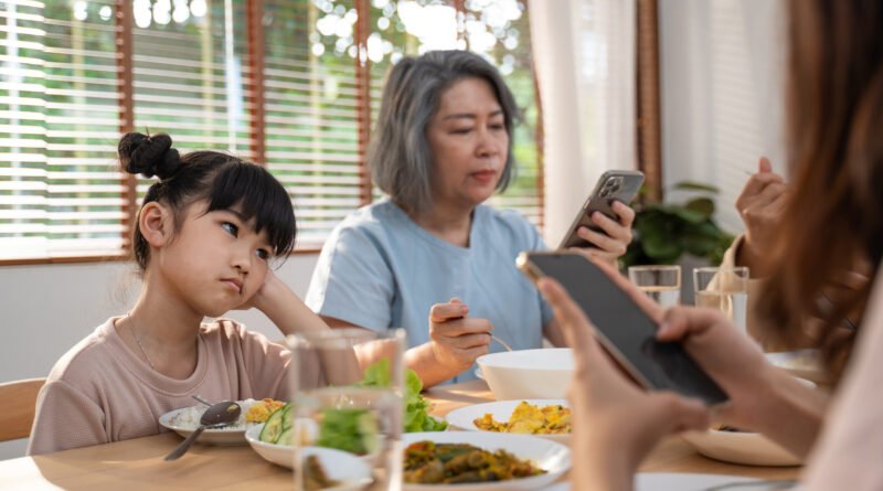 uso del celular: familia absorta en el teléfono en la mesa mientras una adolescente se aburre