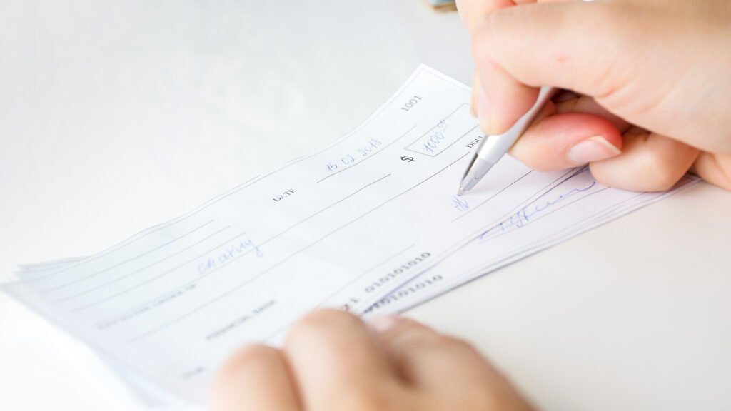 cheques rechazados: una persona firma un cheque bancario con lapicera