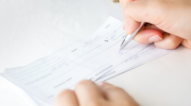 cheques rechazados: una persona firma un cheque bancario con lapicera