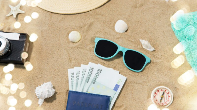 déficit turístico: pasaporte, cámara y anteojos sobre la arena de la playa
