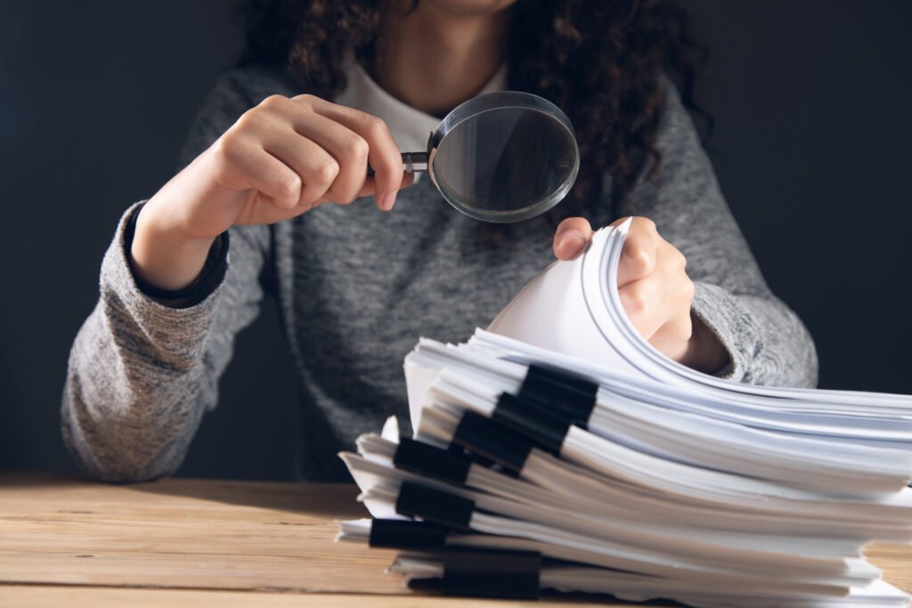delitos económicos: auditora con lupa revisando documentos financieros