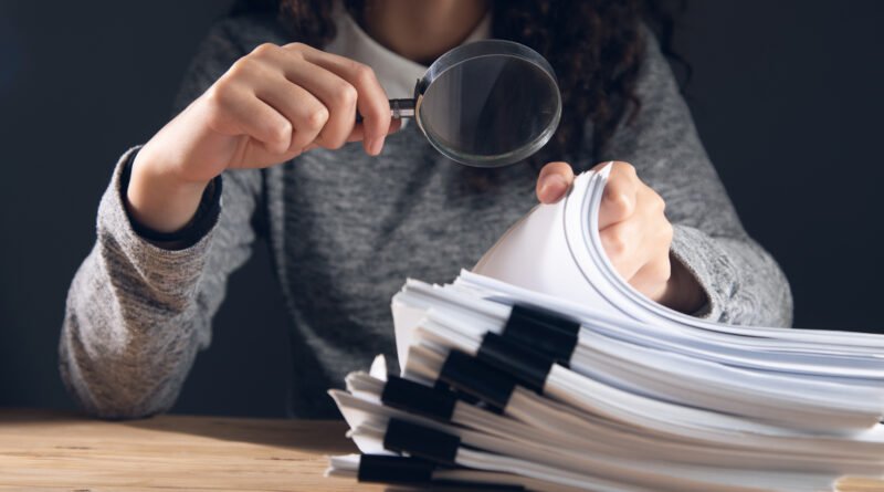 delitos económicos: auditora con lupa revisando documentos financieros