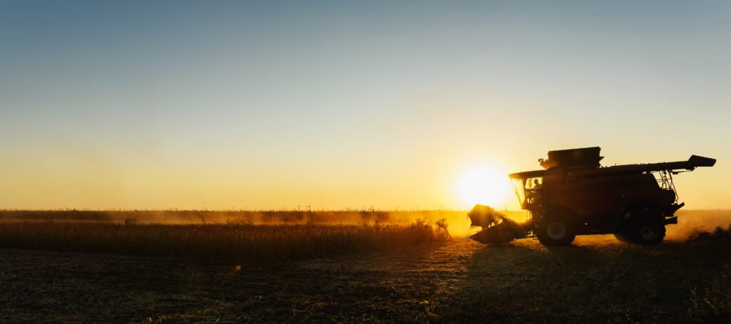 exportaciones del agro: cosechadora trabajando en un campo de soja al atardecer