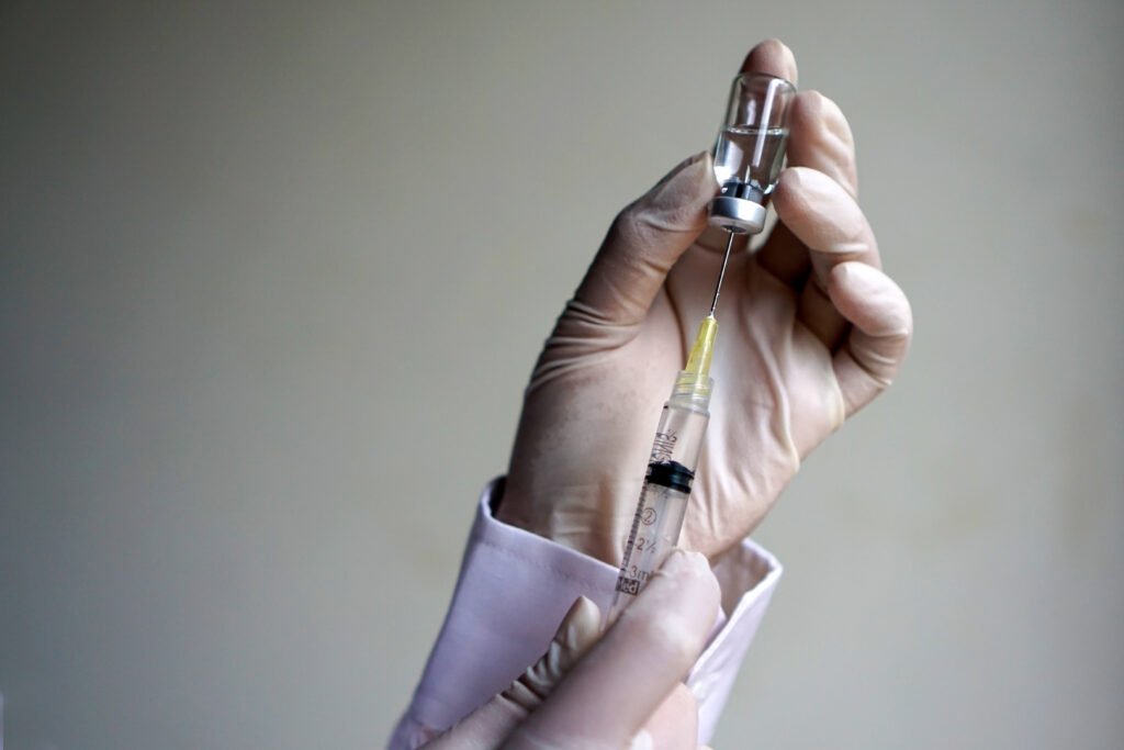 vacuna del dengue: mano con guante sostiene un vial de vacuna y una jeringa
