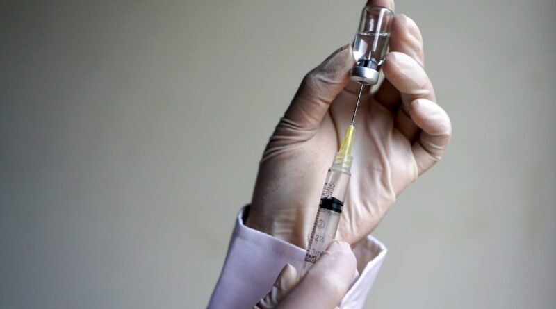 vacuna del dengue: mano con guante sostiene un vial de vacuna y una jeringa