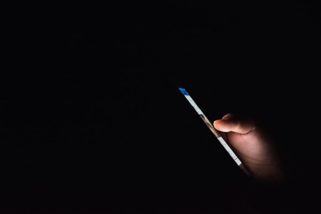mano con un celular iluminado en la oscuridad, desnudos con IA