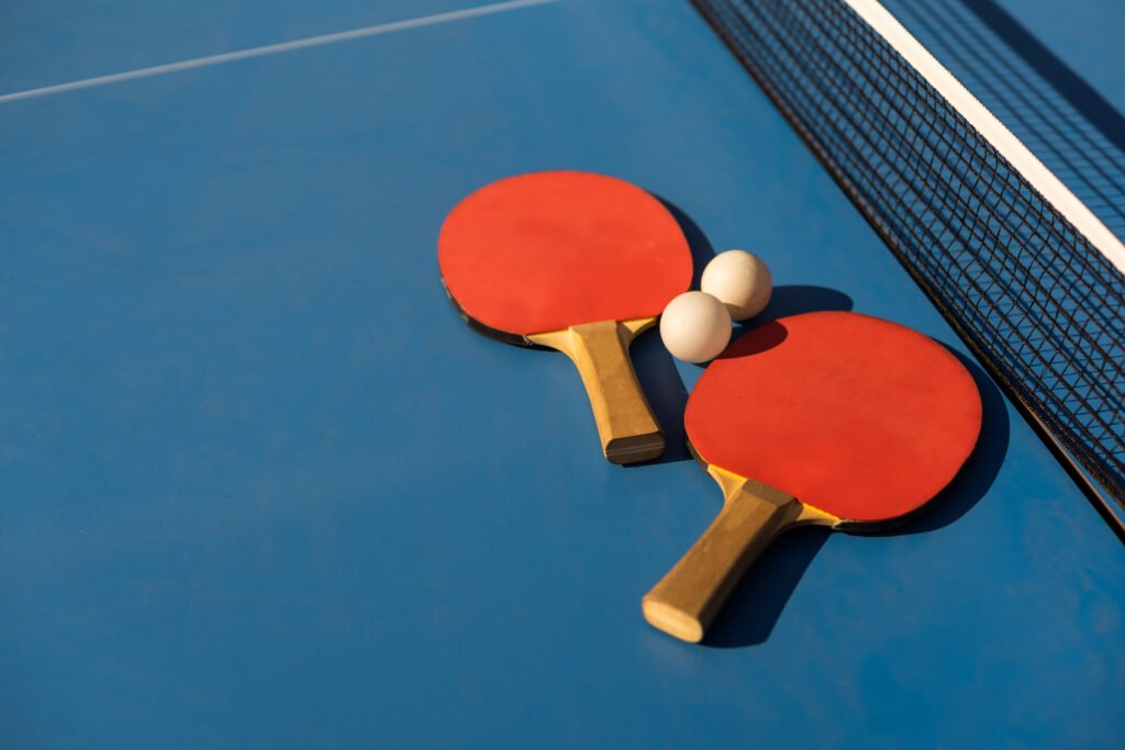 tenis de mesa: paletas y pelota blanca sobre una mesa de ping pong azul