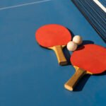 tenis de mesa: paletas y pelota blanca sobre una mesa de ping pong azul