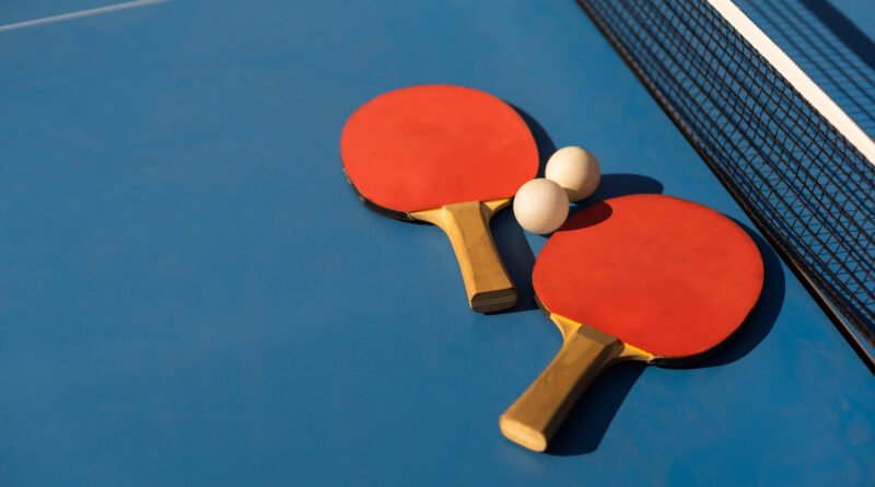 tenis de mesa: paletas y pelota blanca sobre una mesa de ping pong azul